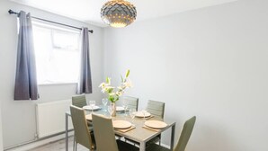Un comedor con una mesa dispuesta para cuatro, sillas, un jarrón con flores y una lámpara colgante esférica original.