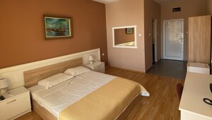 A hotel room with a large bed, a bedside table with a lamp, a painting on the wall, a mirror, a wardrobe, and a desk with a chair. - Hotel NOY (Varna)