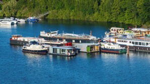 En småbåtshamn med olika typer av båtar förtöjda, omgiven av ett skogsområde.