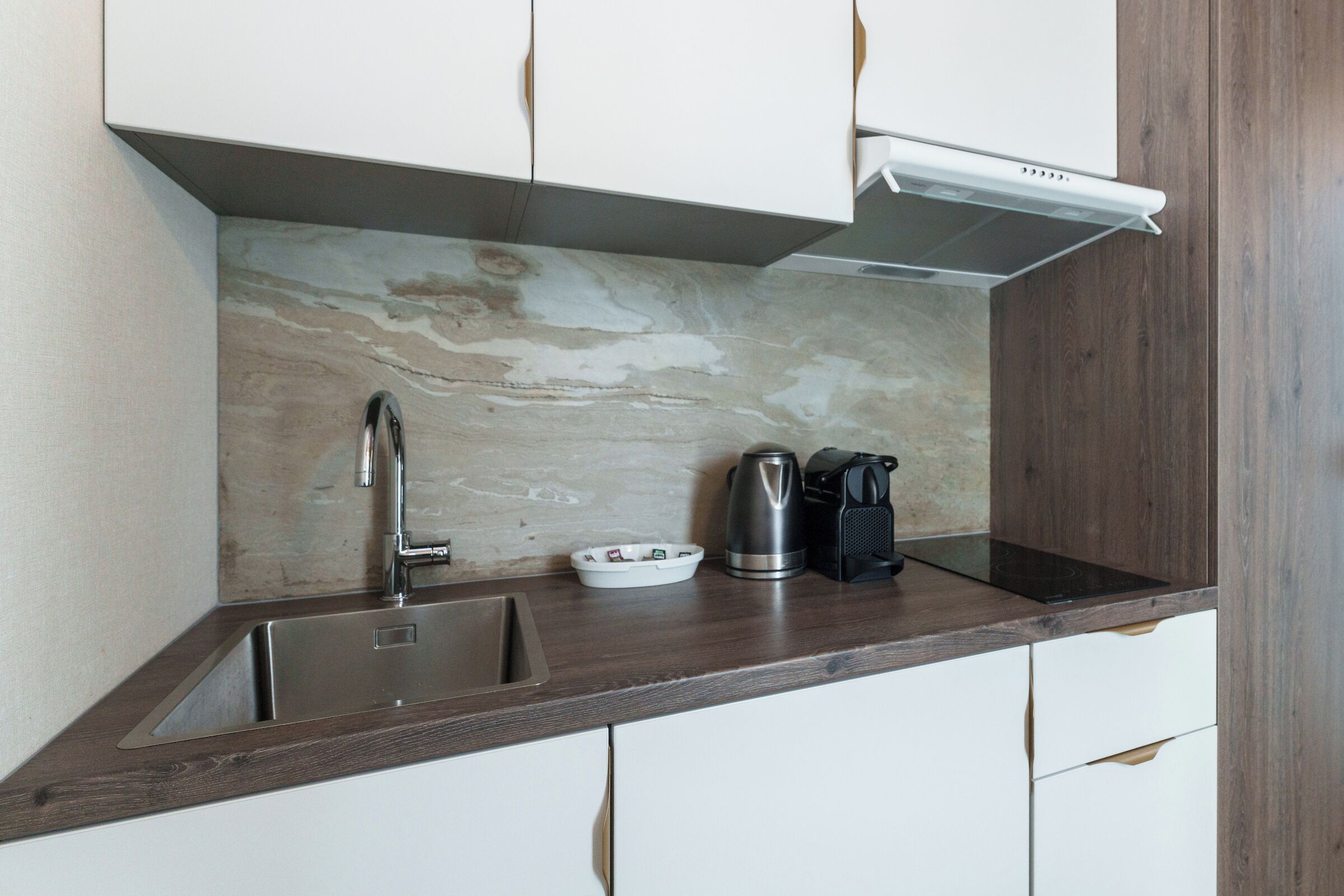A kitchen with a stainless steel sink, a coffee maker, and a kettle on the countertop.