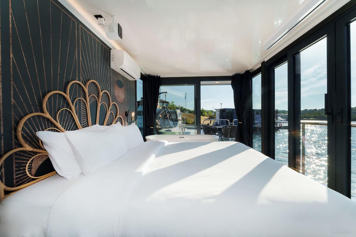 Un dormitorio moderno con una cama grande, un muro de vidrio y vista al agua.