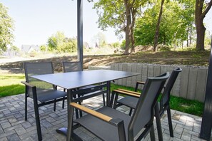 Eine Terrassengruppe mit Tisch und Stühlen, umgeben von einer niedrigen Steinmauer und viel Grün.