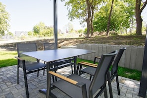 Eine Terrassengruppe mit Tisch und Stühlen, umgeben von einer niedrigen Steinmauer und viel Grün.