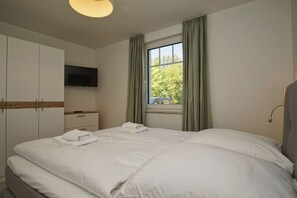 Ein Hotelzimmer mit Bett, Fernseher, Kleiderschrank und einem Fenster mit Vorhängen.