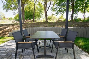 A covered outdoor dining area with a rectangular table and six chairs, surrounded by a wooden fence and trees. - Beachfront vacation rental with a terrace, pool access, and a sauna - Rex Rugia - Rex (Göhren)