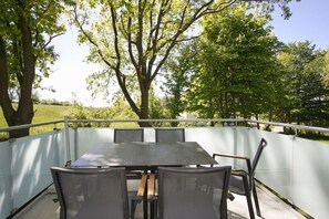 An outdoor patio with a table and chairs, surrounded by a white fence, and trees in the background. - Beachfront vacation rental with a balcony, pool access, and a sauna - Rex Rugia - Rex Rugia (Göhren)