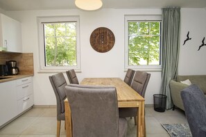 A modern kitchen with a wooden dining table and chairs, large windows with curtains, and a wall clock. - Beachfront vacation rental with a balcony, pool access, and a sauna - Rex Rugia - Rex Rugia (Göhren)