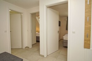 A hallway with white walls and doors leading to a bedroom with a bed and a bedside table. - Beachfront vacation rental with a balcony, pool access, and a sauna - Rex Rugia - Rex Rugia (Göhren)