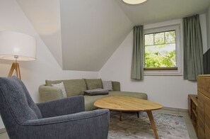 A cozy room with a grey armchair, a green sofa, a wooden coffee table, and a window with curtains. - Beachfront vacation rental with a balcony, access to the pool and sauna - Rex Rugia - Rex Rugia (Göhren)