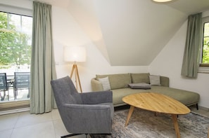 A modern living room with a grey armchair, a green sofa, a wooden coffee table, and a floor lamp. - Beachfront vacation rental with a balcony, access to the pool and sauna - Rex Rugia - Rex Rugia (Göhren)