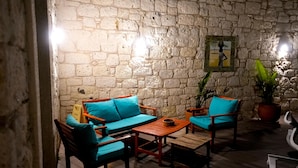 A stone-walled room with a wooden sofa, two chairs, a small table, and a potted plant. - Kiva Alaçatı Hotel By Amarillo  (Cesme)