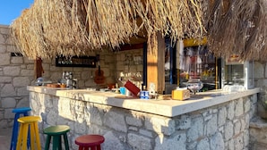 A stone building with a thatched roof, a bar area with stools, and a Red Bull refrigerator. - Kiva Alaçatı Hotel By Amarillo  (Cesme)