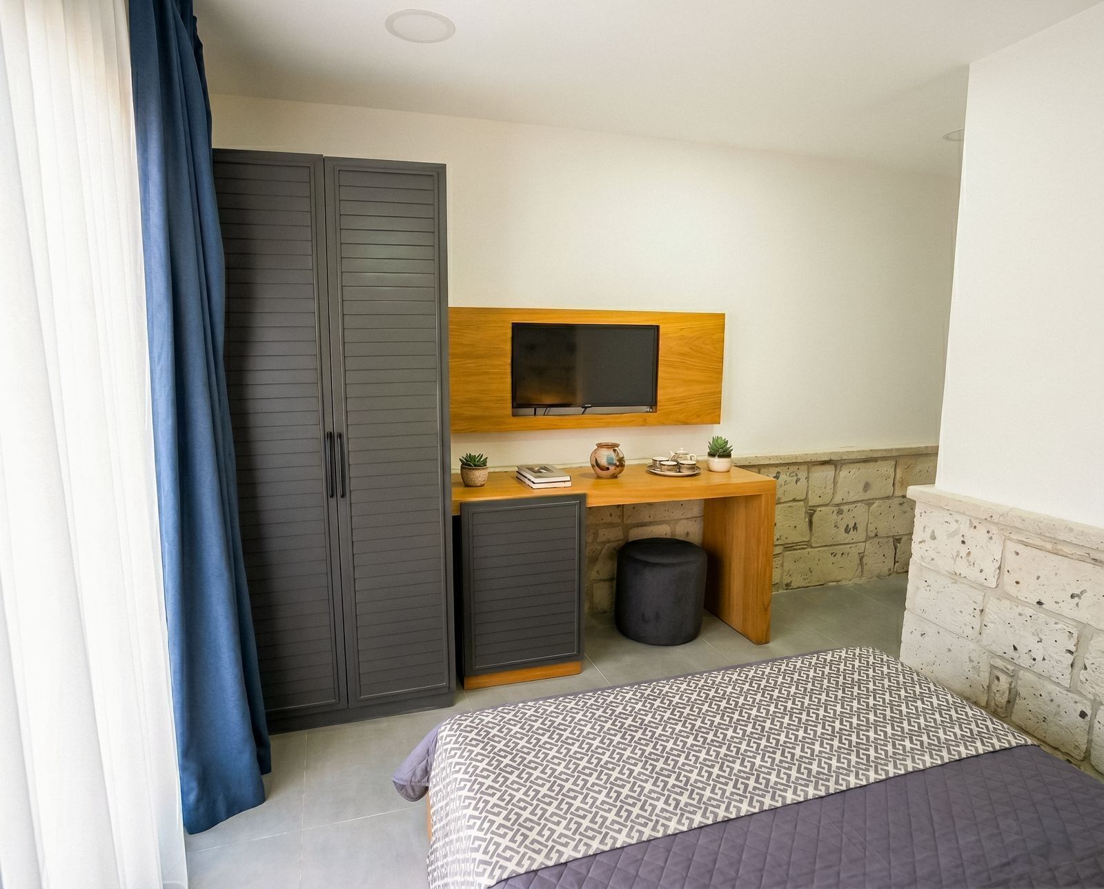 Una habitación pequeña con cama, escritorio, televisión y armario.