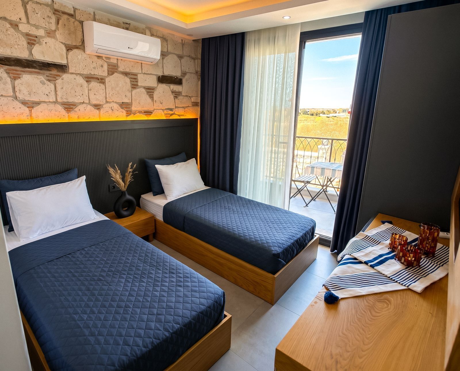 A hotel room with two beds, a wooden headboard, a balcony with a view, and an air conditioning unit on the wall.