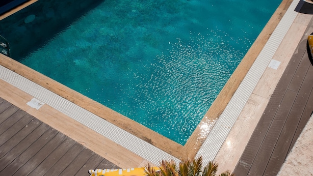 A clear blue pool with a wooden deck and a tiled walkway. - Kiva Alaçatı Hotel By Amarillo  (Cesme)