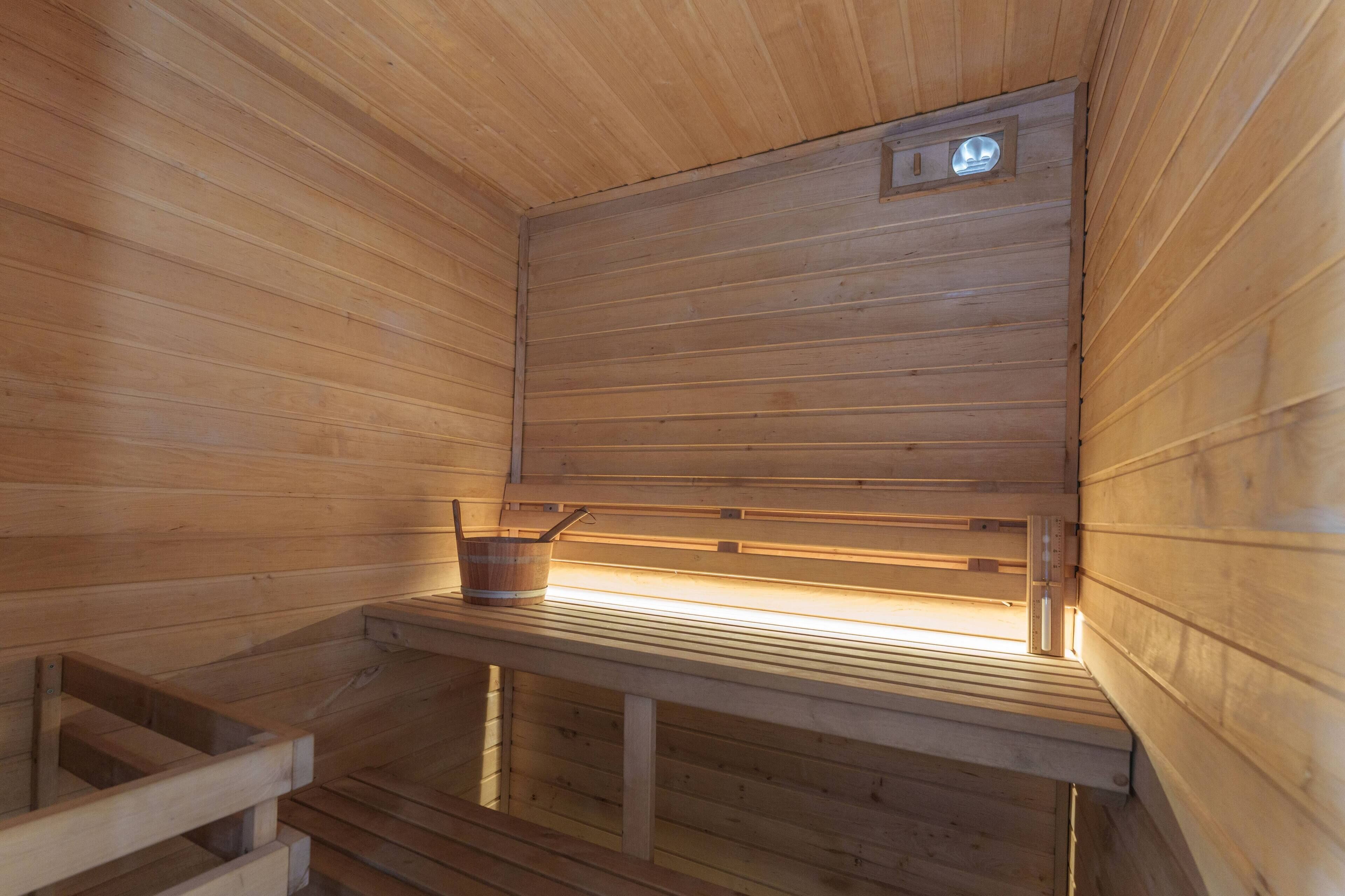 A wooden sauna with benches and a small table with a bucket.