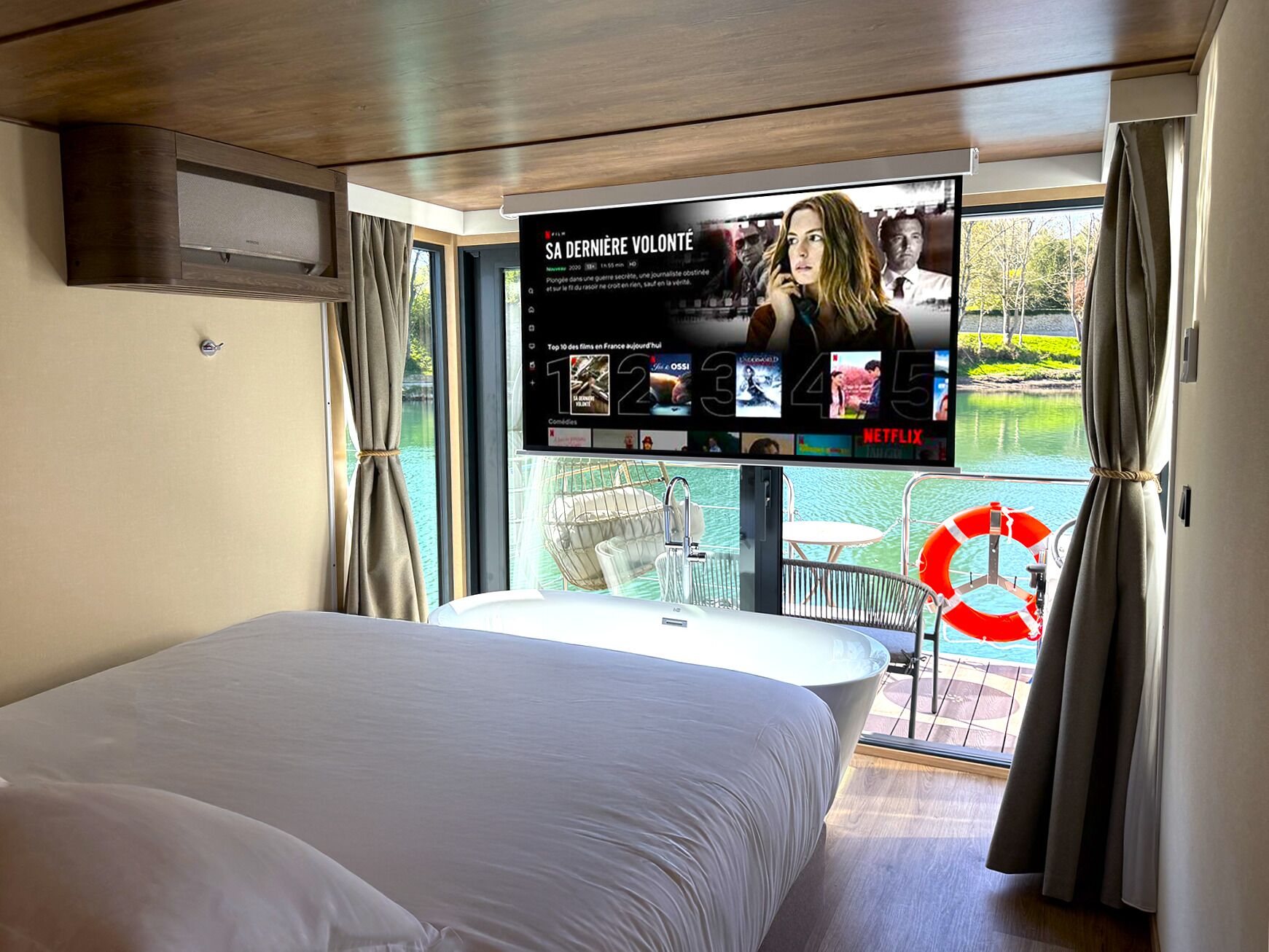 Habitación de hotel moderna con una cama grande, un televisor en la pared mostrando una película, y vista al lago por la ventana.