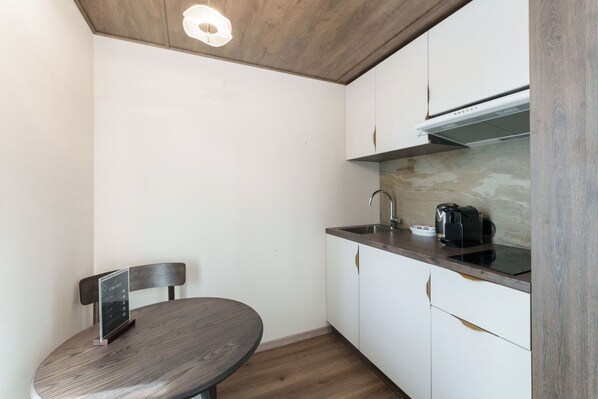 A compact kitchen with white cabinets, a dark countertop, a built-in stove, and a small dining table with a chair.