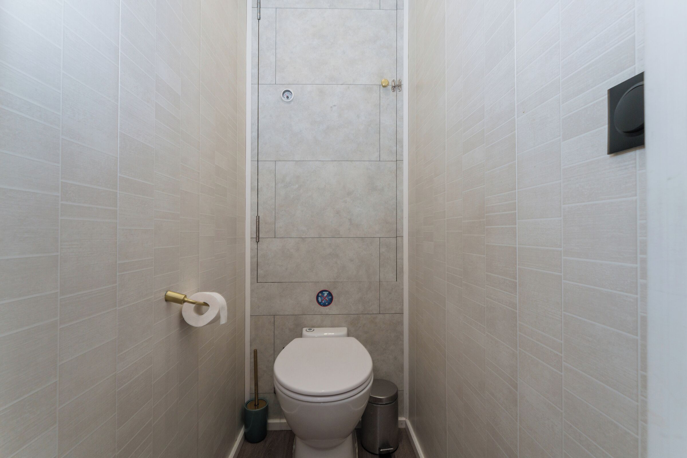 A small, narrow bathroom with a toilet, a trash can, and a toilet paper holder.