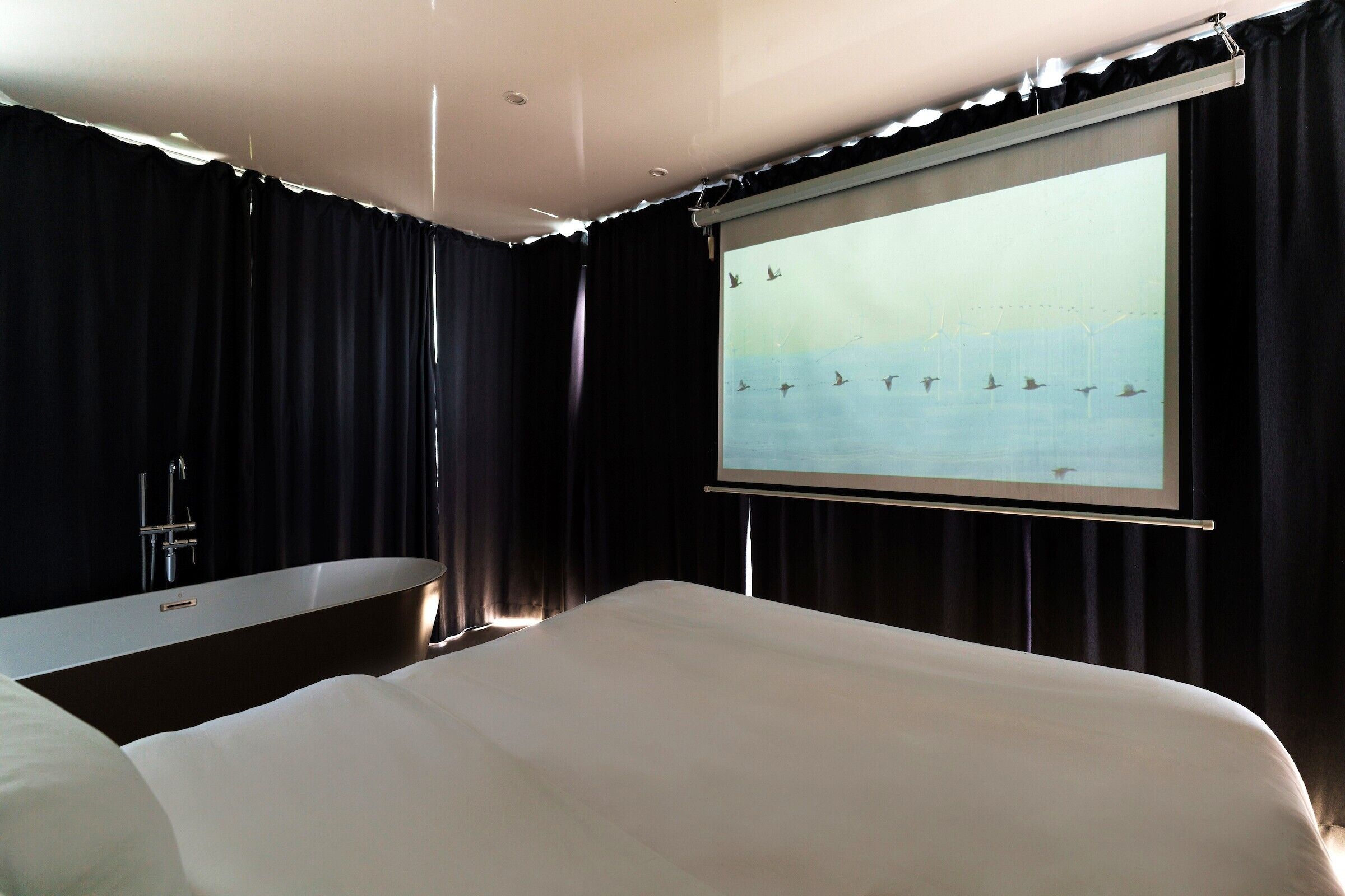 A hotel room with a large bed, a bathtub, and a large window with a view of the sea.