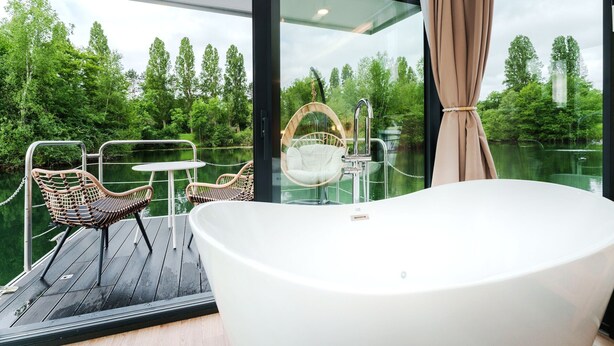 Eine moderne Außenterrasse mit einer großen weißen Badewanne, Korbstühlen und einem Tisch.
