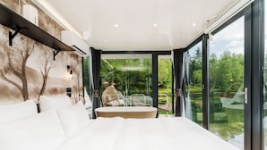 Ein modernes Schlafzimmer mit einem großen Bett, Blick auf einen Garten und einer Glastür zum Außenbereich.
