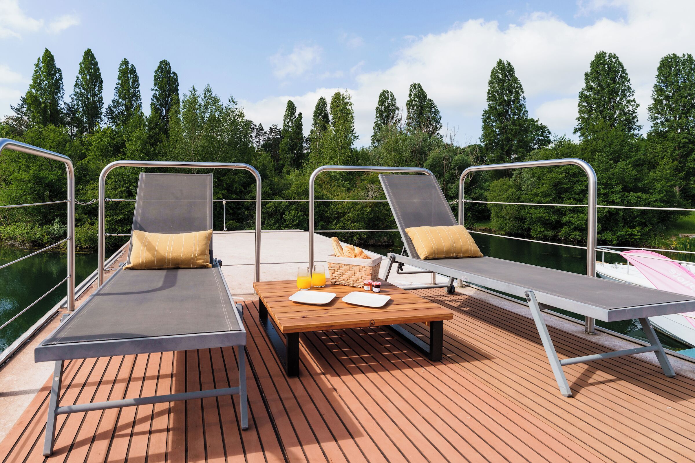 Una terraza con dos sillones, una mesa con una cesta de pan y un vaso de zumo de naranja.