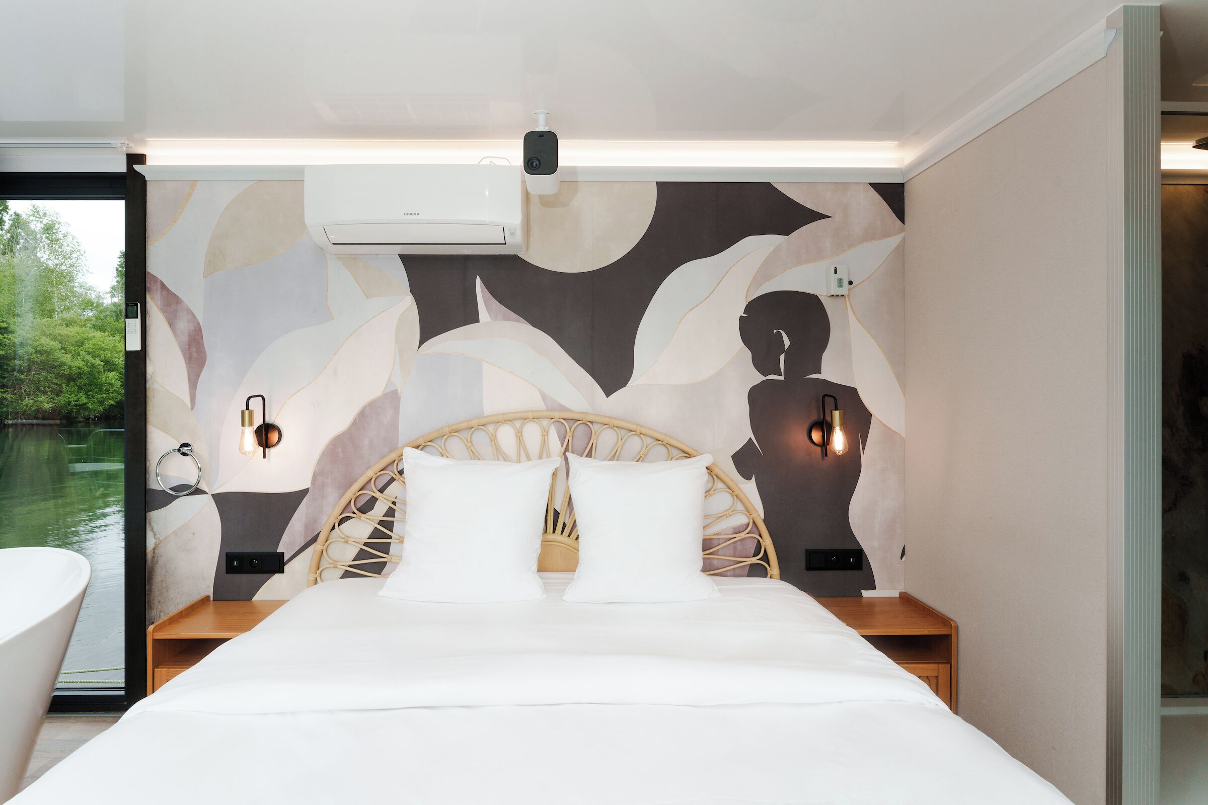 A modern bedroom with a large bed, a wooden headboard, bedside lamps, and a view of a body of water through a glass door.