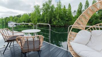 A deck with wicker furniture and a view of a river and trees.