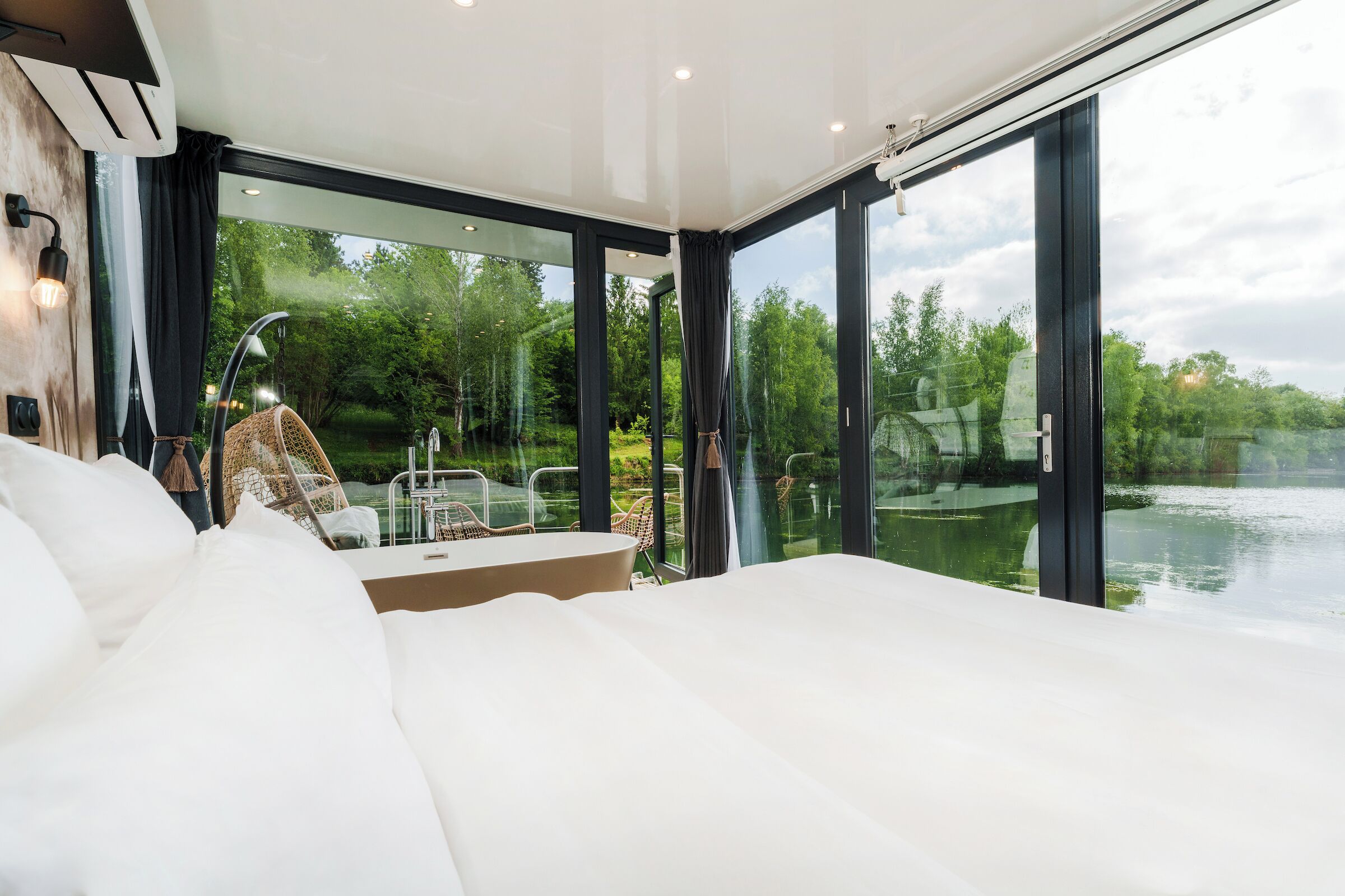 Une chambre moderne avec un grand lit, un mur en verre et une vue sur un lac.