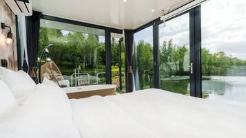 Une chambre moderne avec un grand lit, un mur en verre et une vue sur un lac.