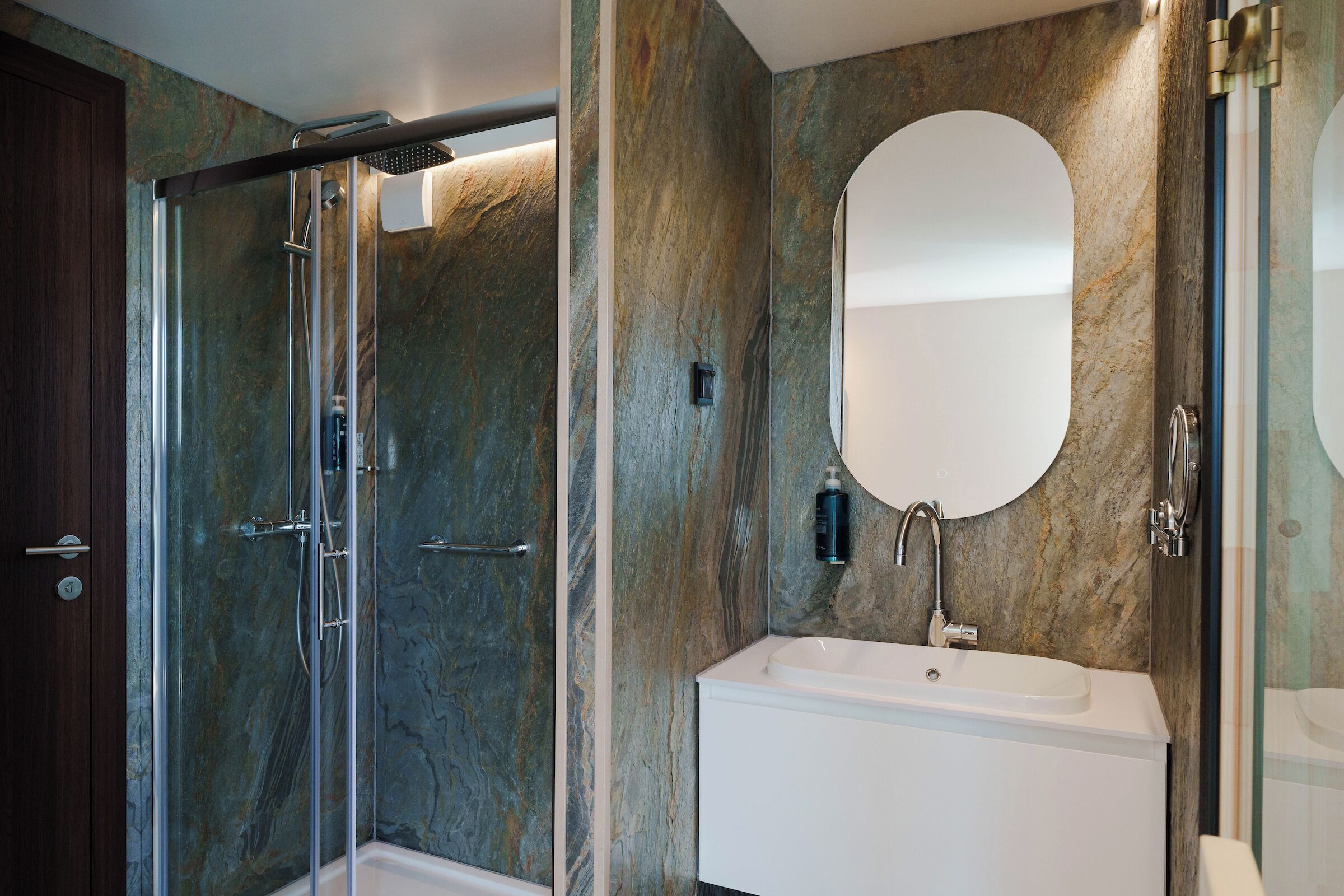 Un baño moderno con ducha envuelta en vidrio, un lavabo blanco y un espejo grande.
