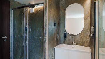 Un baño moderno con ducha envuelta en vidrio, un lavabo blanco y un espejo grande.