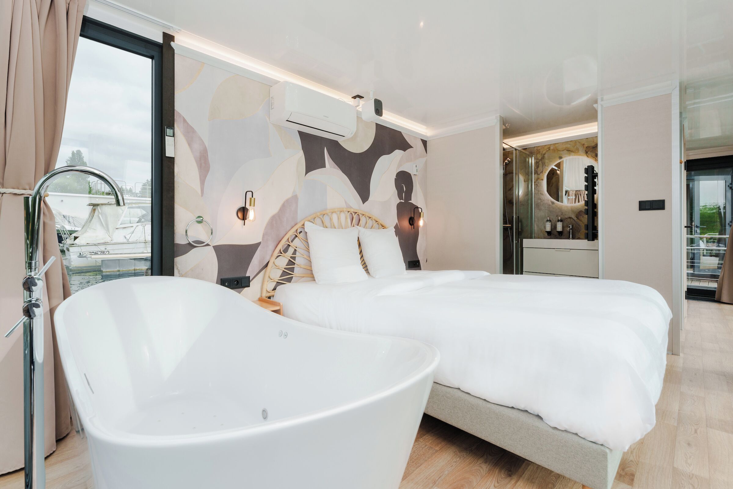 Een moderne slaapkamer met een groot bed, een vrijstaand bad en een badkamer met een spiegel en wastafel.