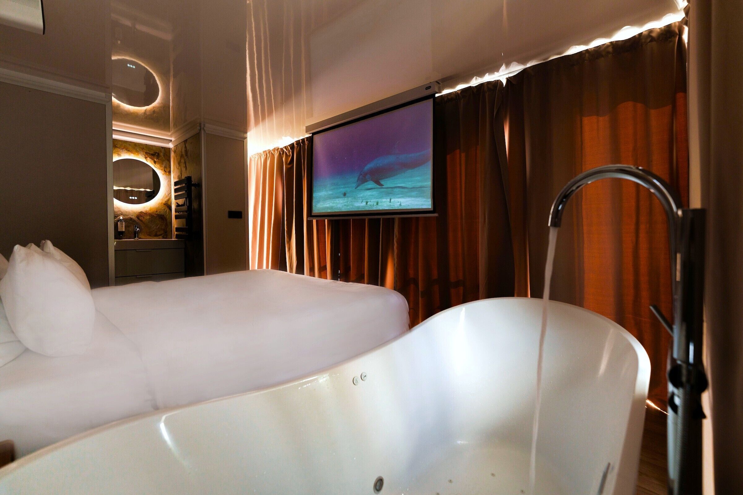 Ein Hotelzimmer mit einer großen Badewanne, einem an der Wand befestigten Fernseher und einem Spiegel über der Badewanne.