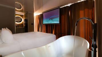 Ein Hotelzimmer mit einer großen Badewanne, einem an der Wand befestigten Fernseher und einem Spiegel über der Badewanne.