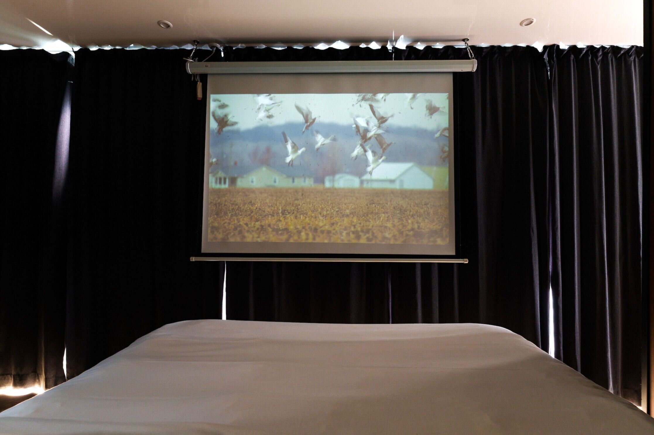 Una pantalla de proyección en una habitación con cama y cortinas oscuras.