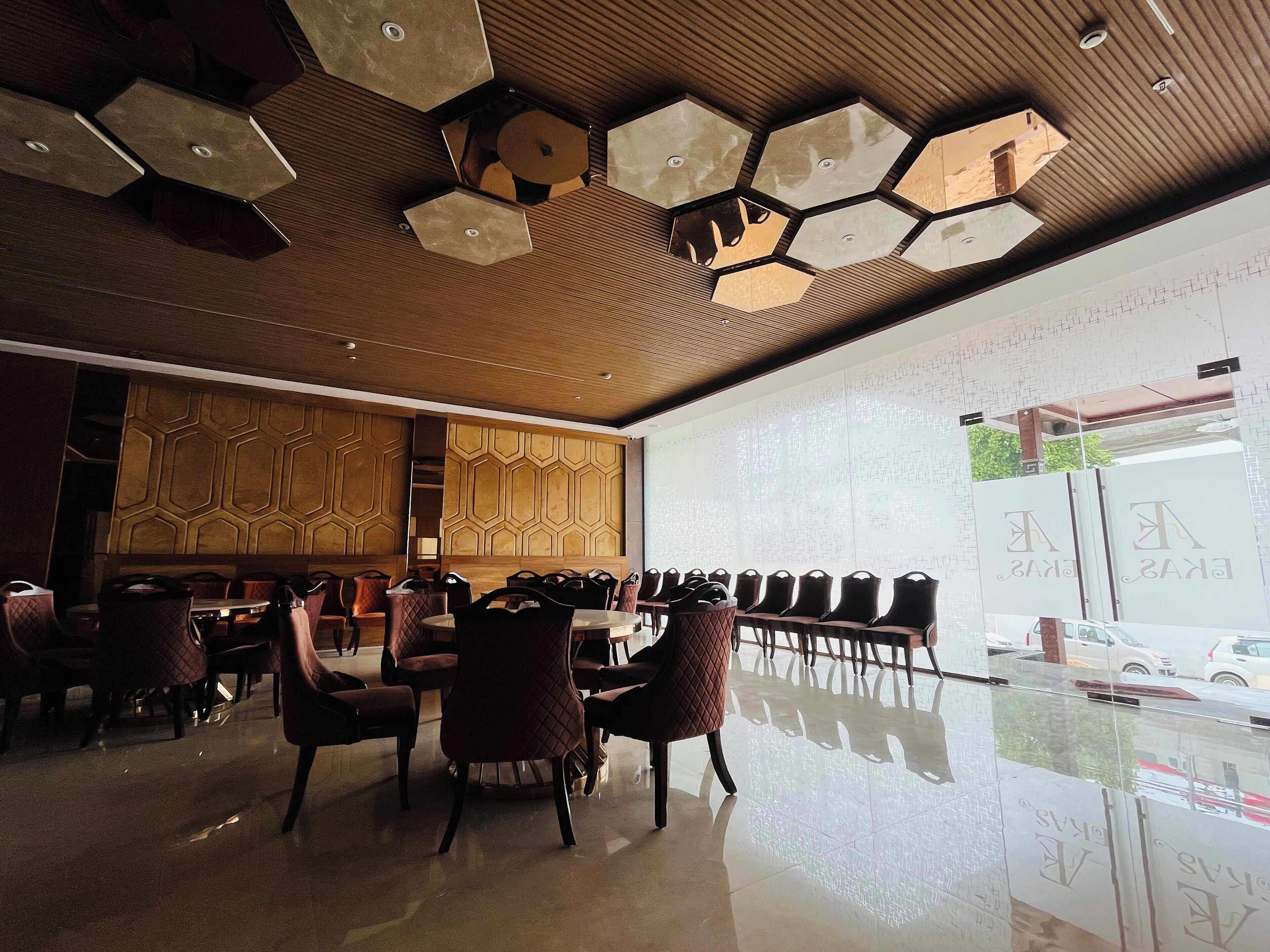 A modern dining area with hexagonal ceiling lights, a long table with chairs, and a view of the street through a glass wall.