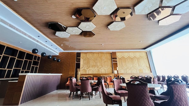 A modern interior with hexagonal ceiling lights, wooden paneling, and a seating area with cushioned chairs and tables.