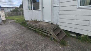 Een wit gebouw met een houten hellingbaan die naar een deur leidt.