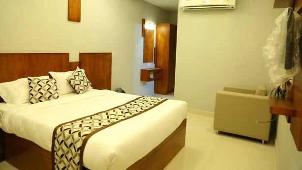A hotel room with a large bed, an air conditioning unit, a small seating area, and a wooden headboard. - 4 U BUSINESS CLASS (Chennai)