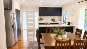 A modern kitchen with dark cabinets, a stainless steel refrigerator, a dining table with wooden chairs, and a clock on the wall. - Horizon Loft by Ready Set Stay (Cowes)