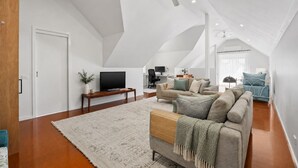 A spacious loft with a high ceiling, a large window, a cozy seating area with a sofa and armchair, and a flat-screen TV. - Horizon Loft by Ready Set Stay (Cowes)