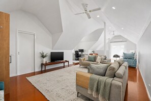 Un loft spacieux avec un haut plafond, une grande fenêtre, un coin salon confortable avec un canapé et un fauteuil, et un téléviseur à écran plat.