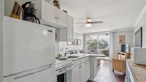 A modern kitchen with white cabinets, a stove, and a sink. There is a ceiling fan and a window with a view of the outdoors.