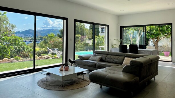 A modern living room with large windows, a grey sofa, a coffee table, and a view of a pool and garden. - Beautiful Villa Moderne in Marseille close to all tourist attractions (Unknown)