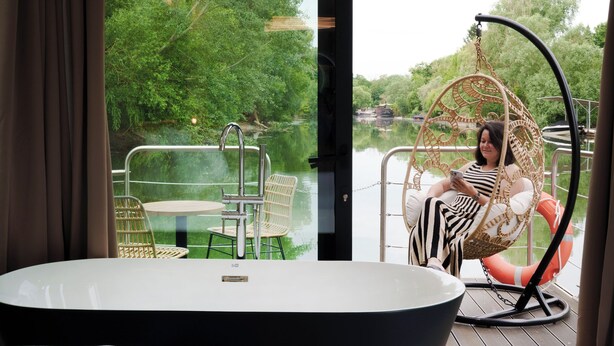 A room with a large bathtub, a wicker chair, and a table with chairs. - L'Escale Royale Poissy Ile de Migneaux (Poissy)