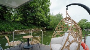 A deck with wicker furniture, including a hanging chair and two chairs, overlooking a river. - L'Escale Royale Poissy Ile de Migneaux (Poissy)