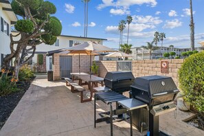 An outdoor patio with a grill, tables, and umbrellas.