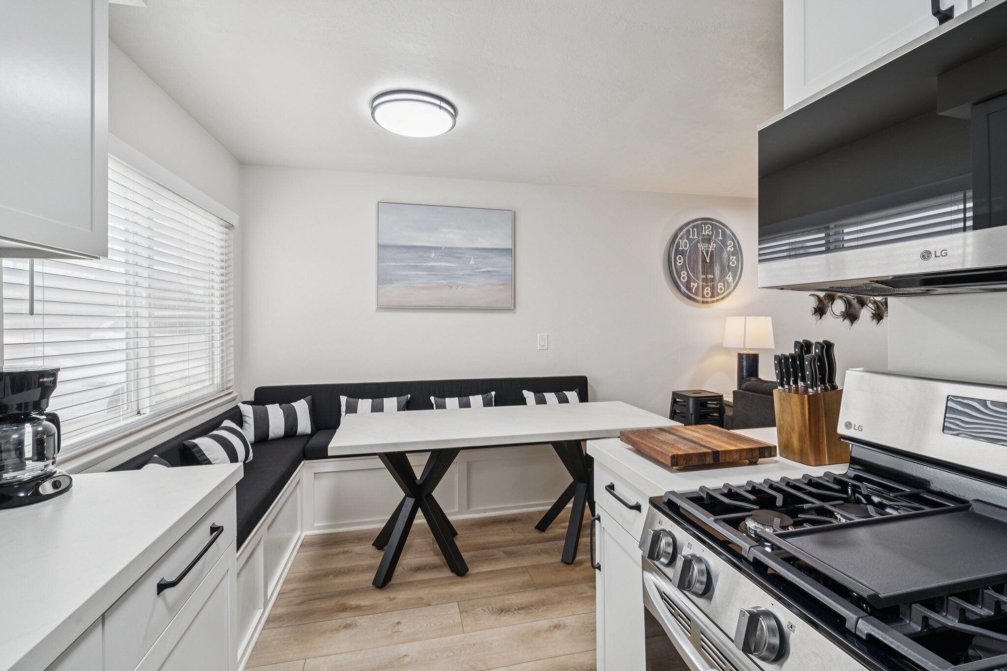 A modern kitchen with a white countertop, black and white bench seating, a stove, and a wall clock.